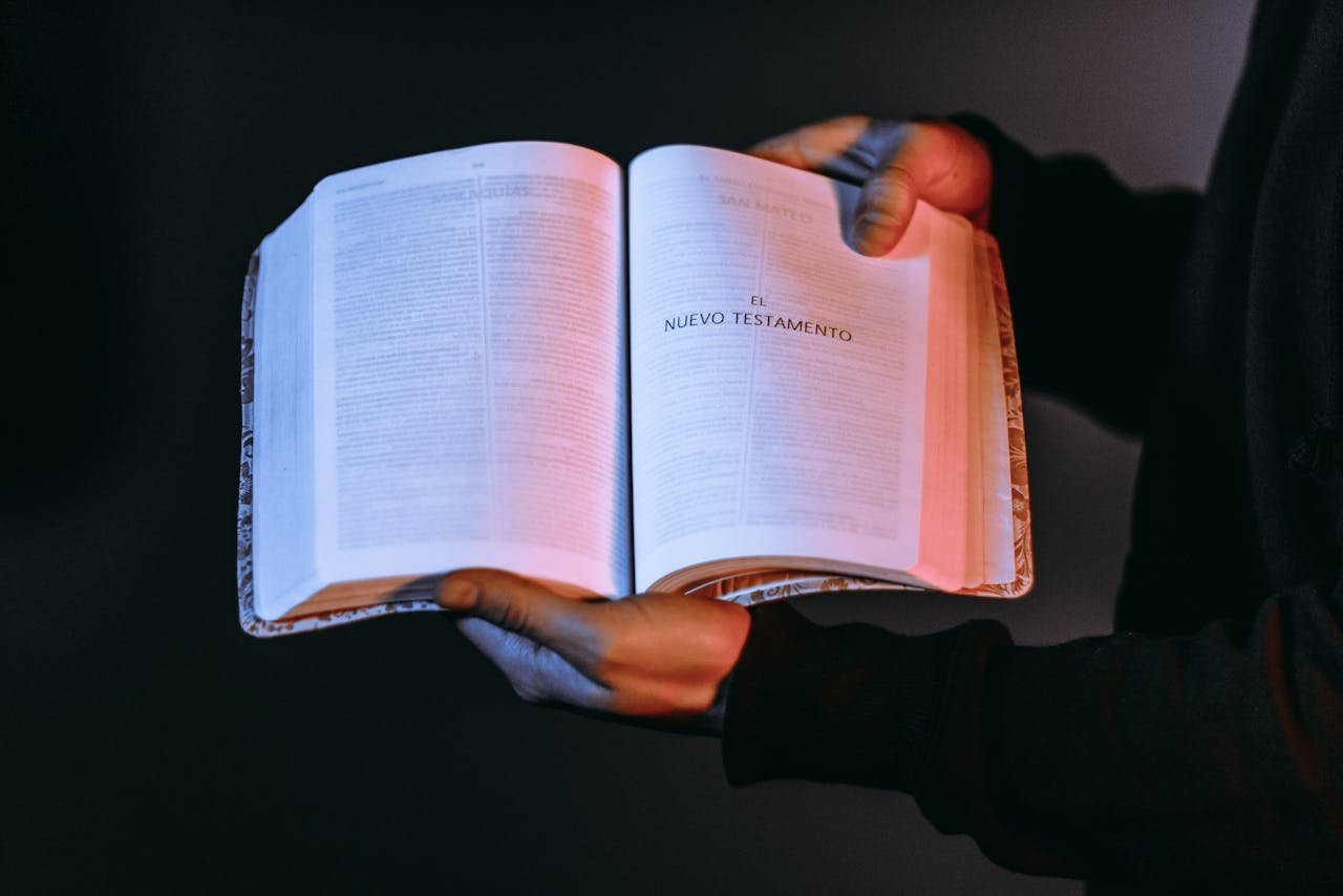 A person holds an open Bible showcasing the New Testament under dramatic lighting.